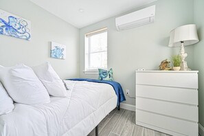 Ein Schlafzimmer mit Bett, Kommode, Fenster mit Jalousien und Wandbildern.