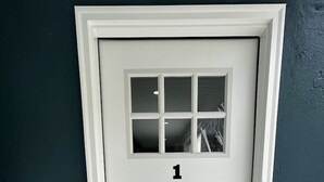 Eine weiße Tür mit der Nummer 1 darüber, ein kleines Fenster und ein Klingel.