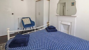 A bedroom with a bed, a chair, a wardrobe, a mirror, and a fireplace. - Harbourside Retreat (Looe)