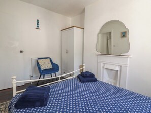 A bedroom with a bed, a chair, a wardrobe, a mirror, and a fireplace. - Harbourside Retreat (Looe)