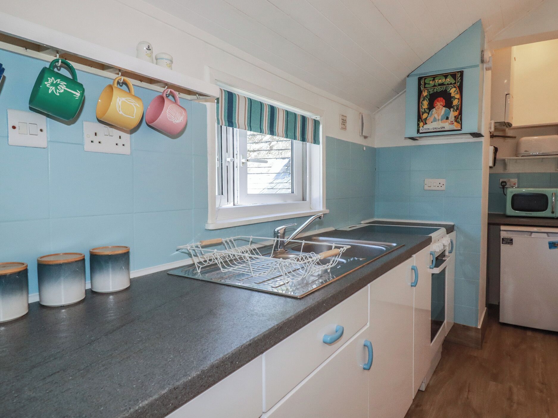 A kitchen with a sink, a dish rack, and a microwave.