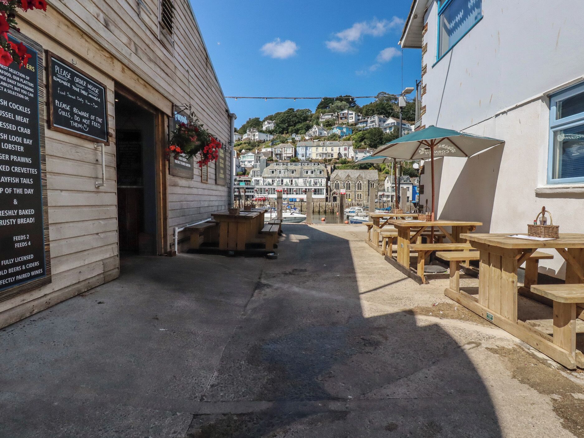 A coastal town with a waterfront café featuring outdoor seating and a menu board.