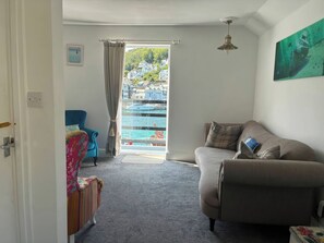 Ein Wohnzimmer mit einer Couch, einem Sessel, einem Fenster mit Blick auf das Wasser und einem Deckenventilator.