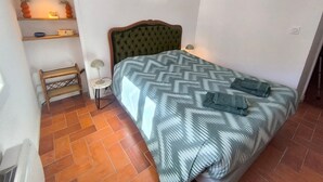 A bedroom with a bed, a bedside table, a lamp, a shelf with decorative items, and a wall-mounted light fixture. - Fajureya House (Vaumeilh)