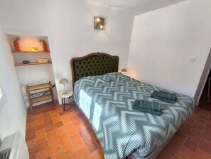 Ein Schlafzimmer mit einem Bett, einem Nachttisch, einer Lampe, einem Regal mit Dekoration und einer Wandleuchte.