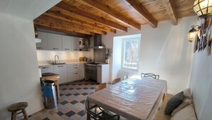 A kitchen with wooden beams, a dining table with chairs, a window, and a radiator. - Fajureya House (Vaumeilh)