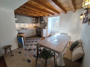 Eine Küche mit Holzbalken, einem Esstisch mit Stühlen, einem Fenster und einer Heizung.