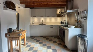 A compact kitchen with white cabinets, a wooden table, and a patterned floor. - Fajureya House (Vaumeilh)