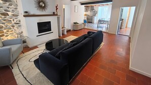 A living room with a fireplace, a sofa, and a dining area in the background. - Fajureya House (Vaumeilh)