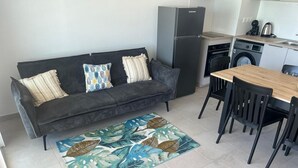A compact living space with a sofa, a dining table with chairs, a kitchen area with a refrigerator, and a washing machine. - Atmosphere and Ocean View (Sainte-Anne)