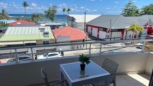 A balcony with a table and chairs, a potted plant, and a view of the street and buildings. - Atmosphere and Ocean View (Sainte-Anne)