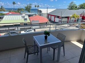 Ein Balkon mit Tisch und Stühlen, einem Blumentopf und Blick auf die Straße und die Häuser.