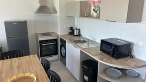 A compact kitchen with a refrigerator, oven, microwave, sink, and a small dining area with a table and chairs. - Atmosphere and Ocean View (Sainte-Anne)