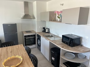 Eine kompakte Küche mit Kühlschrank, Backofen, Mikrowelle, Spüle und einer kleinen Essecke mit Tisch und Stühlen.