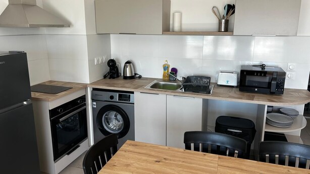 A compact kitchen with a washing machine, a coffee maker, and a microwave. - Atmosphere and Ocean View (Sainte-Anne)