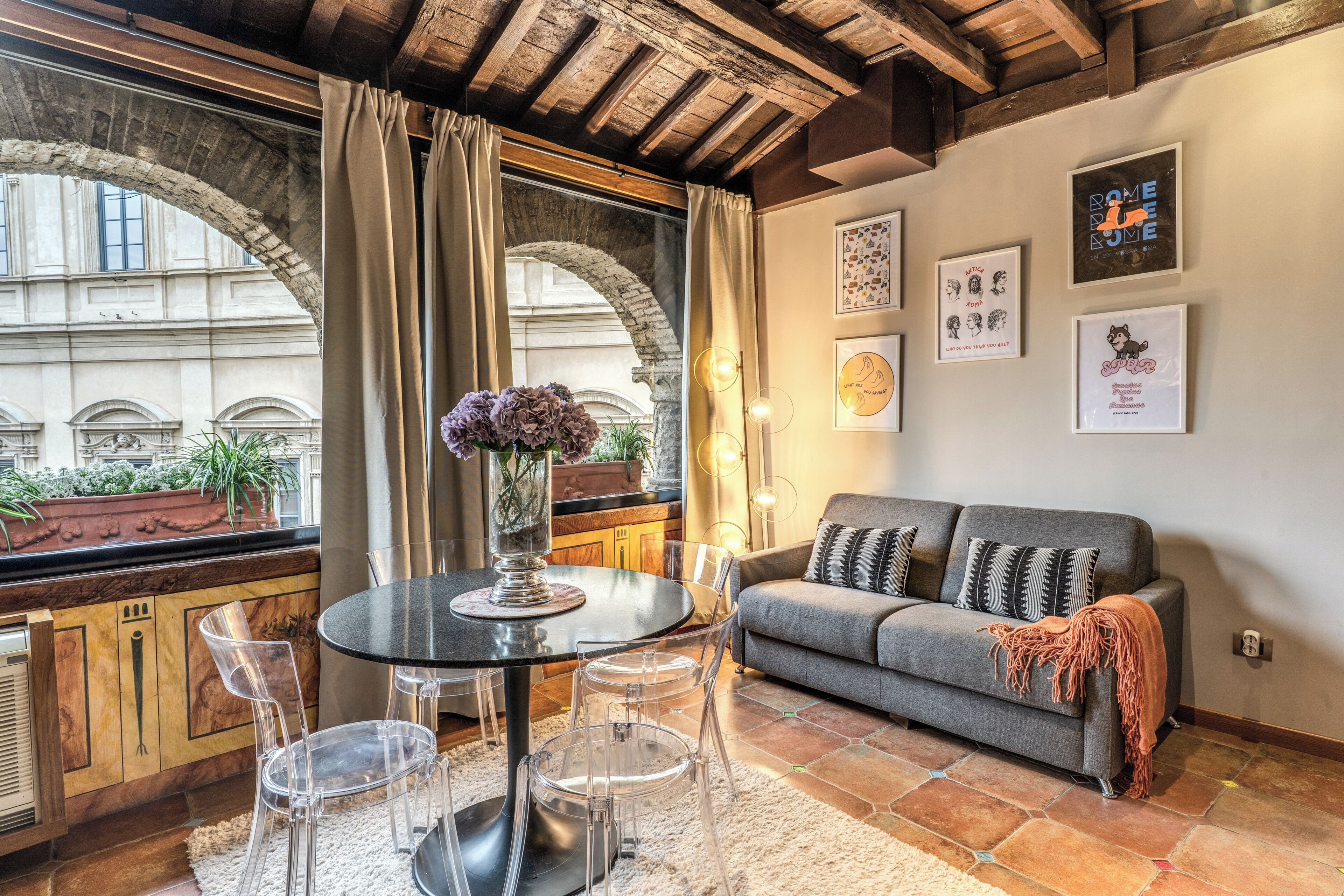 Una sala de estar acogedora con un sofá gris, sillas traslúcidas, una mesa redonda con un florero y obras de arte en las paredes.