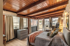 A bedroom with a wooden ceiling, a bed with a quilted blanket, a dresser, and a window with curtains. - Imperiale Luxury Home (Roma)
