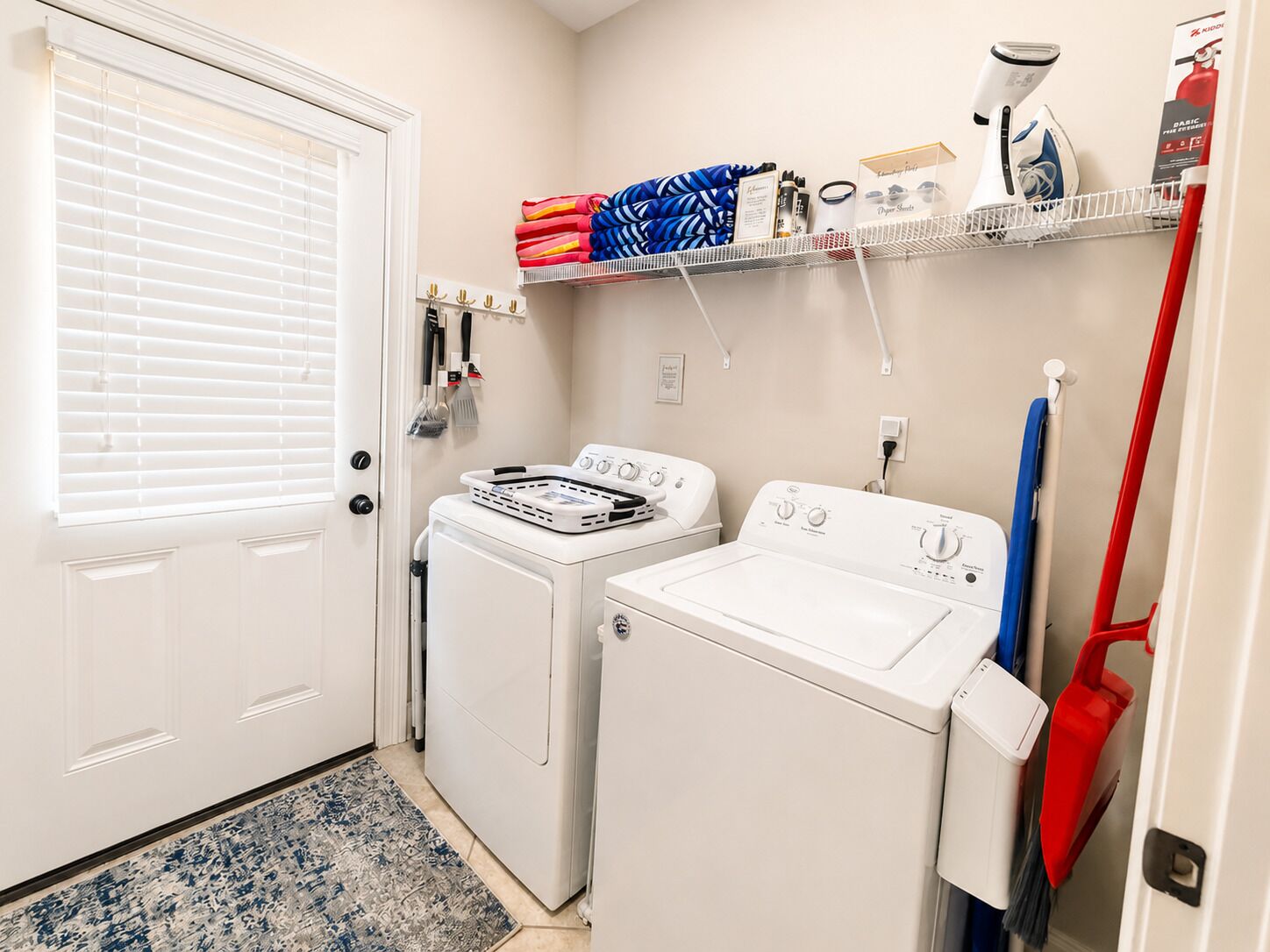 A laundry room with a washing machine, dryer, ironing board, and various cleaning supplies.