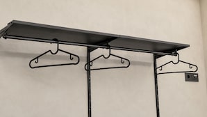Un estante de metal con tres colgadores negros sobre un pared lisa.