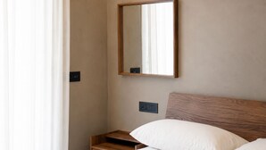 Habitación de hotel con cama, mesita de noche, espejo y toma de corriente.