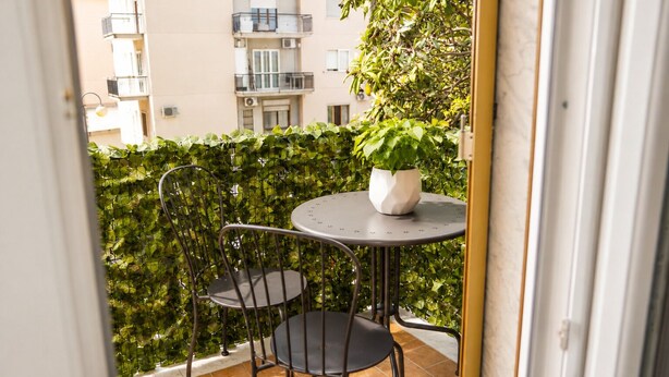 Un balcón con una mesa redonda y dos sillas, una planta en maceta y una valla de metal.