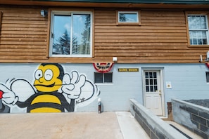 Un edificio con fachada de madera, un letrero que dice 'GAME ROOM' y un mural de una abeja.