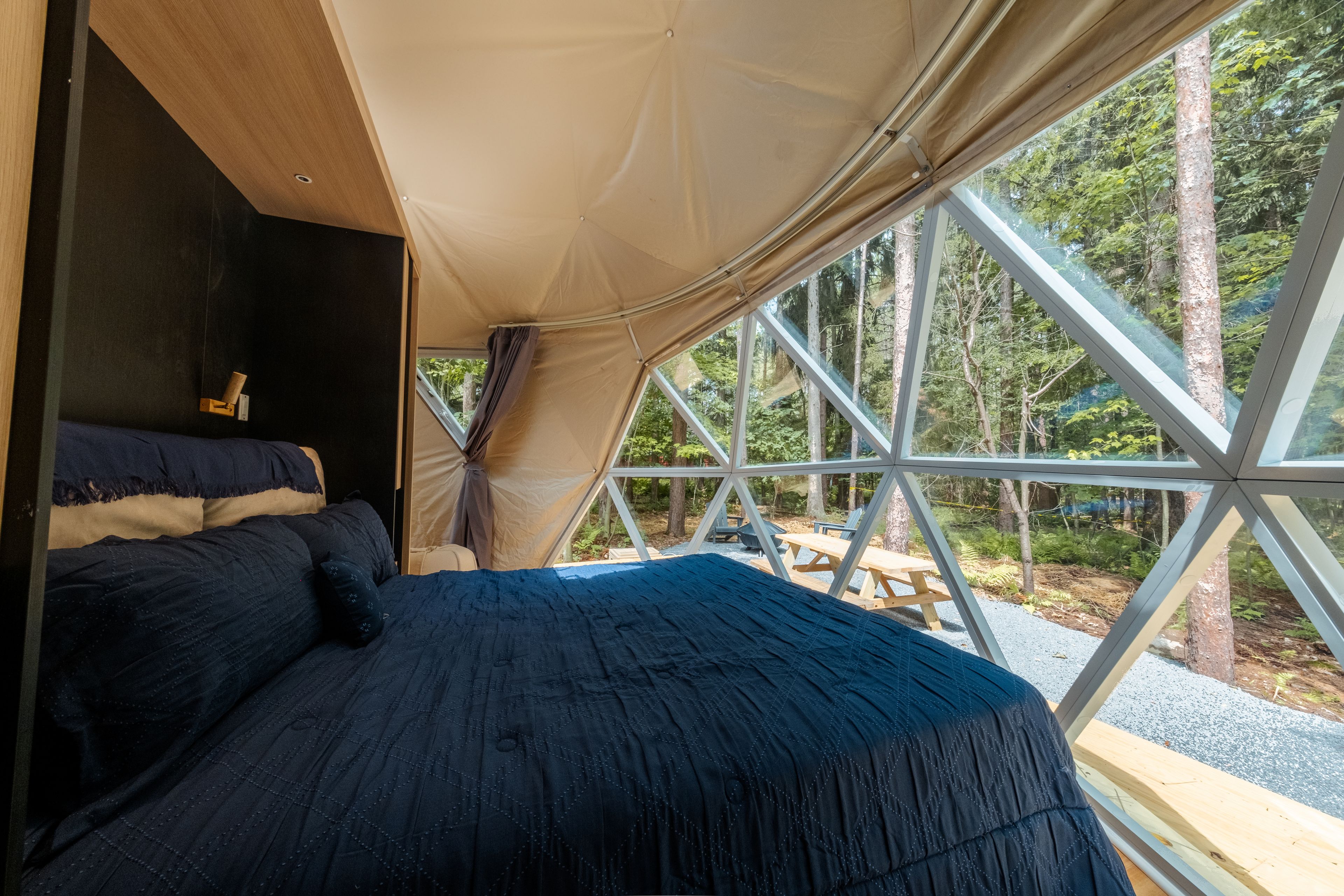 A tented accommodation with a bed, a table, and a view of the forest.