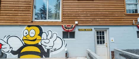 A building with a wooden facade, a 'GAME ROOM' sign, and a mural of a bee.