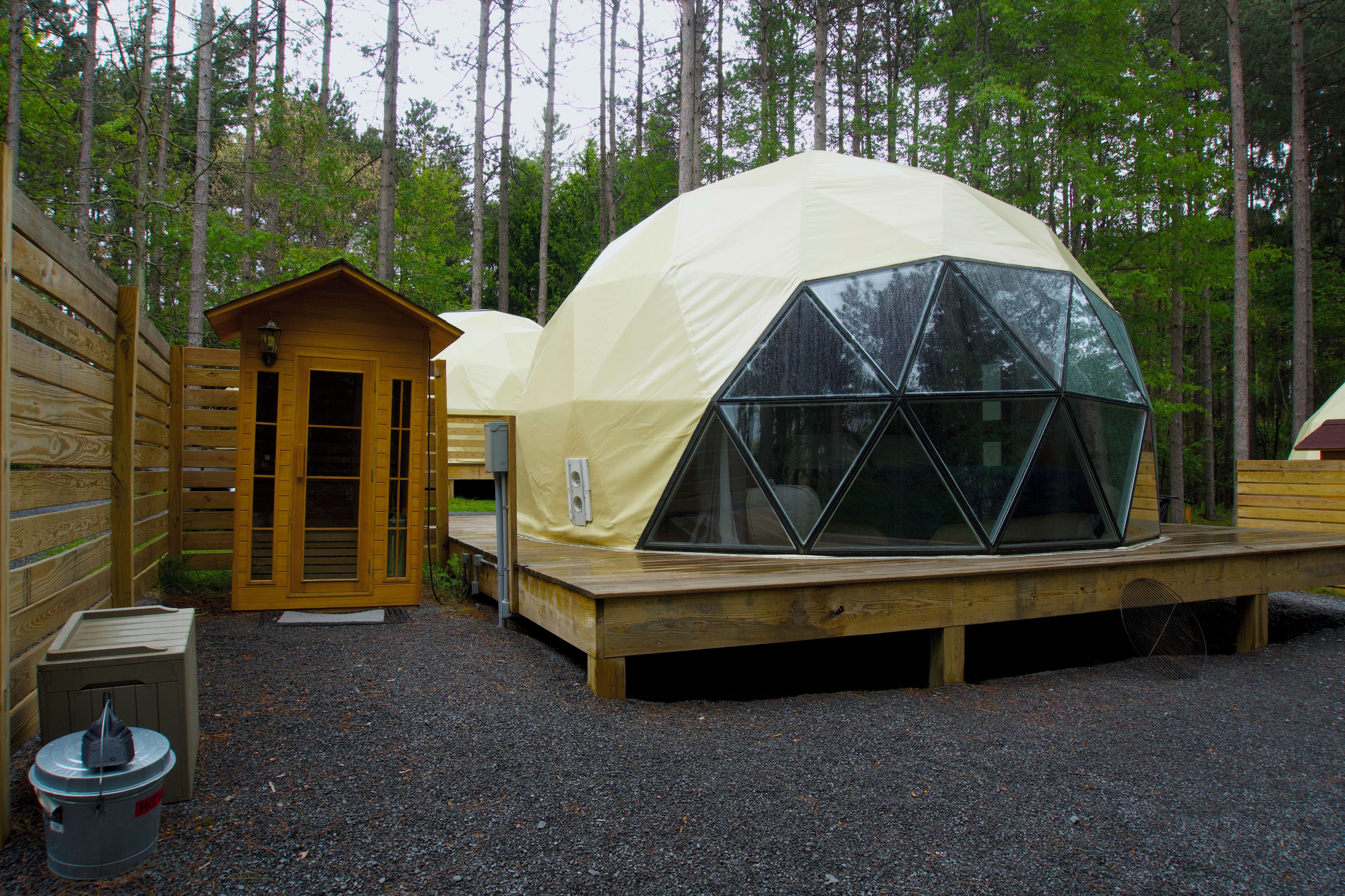 A geodesic dome structure with a wooden deck and a small wooden building adjacent to it.