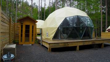A geodesic dome structure with a wooden deck and a small wooden building adjacent to it.