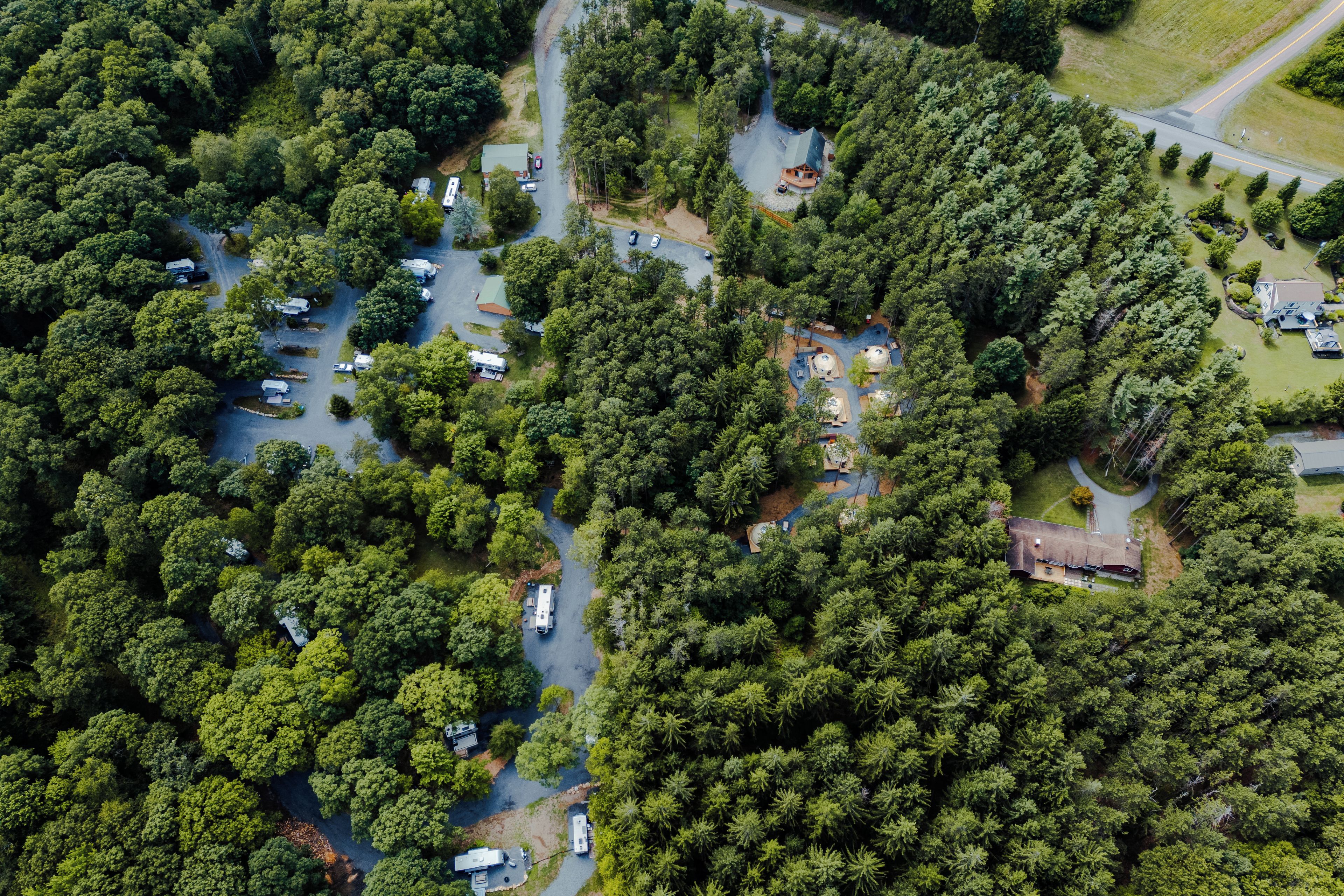 Vista aérea de un camping con vehículos recreativos y tiendas de campaña, rodeado de un bosque denso.