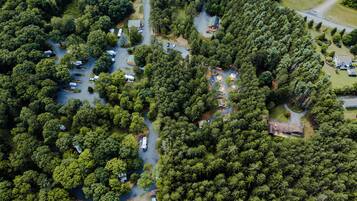 Vista aérea de un camping con vehículos recreativos y tiendas de campaña, rodeado de un bosque denso.