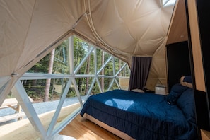 A tent with a bed, a window, and a view of trees. - Beehive Domes at Bumblebee Campground (Accident)