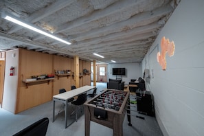 A room with a foosball table, wooden shelves with books, a television, and a fire extinguisher.
