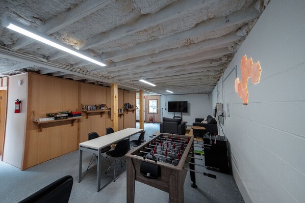 A room with a foosball table, wooden shelves with books, a television, and a fire extinguisher.