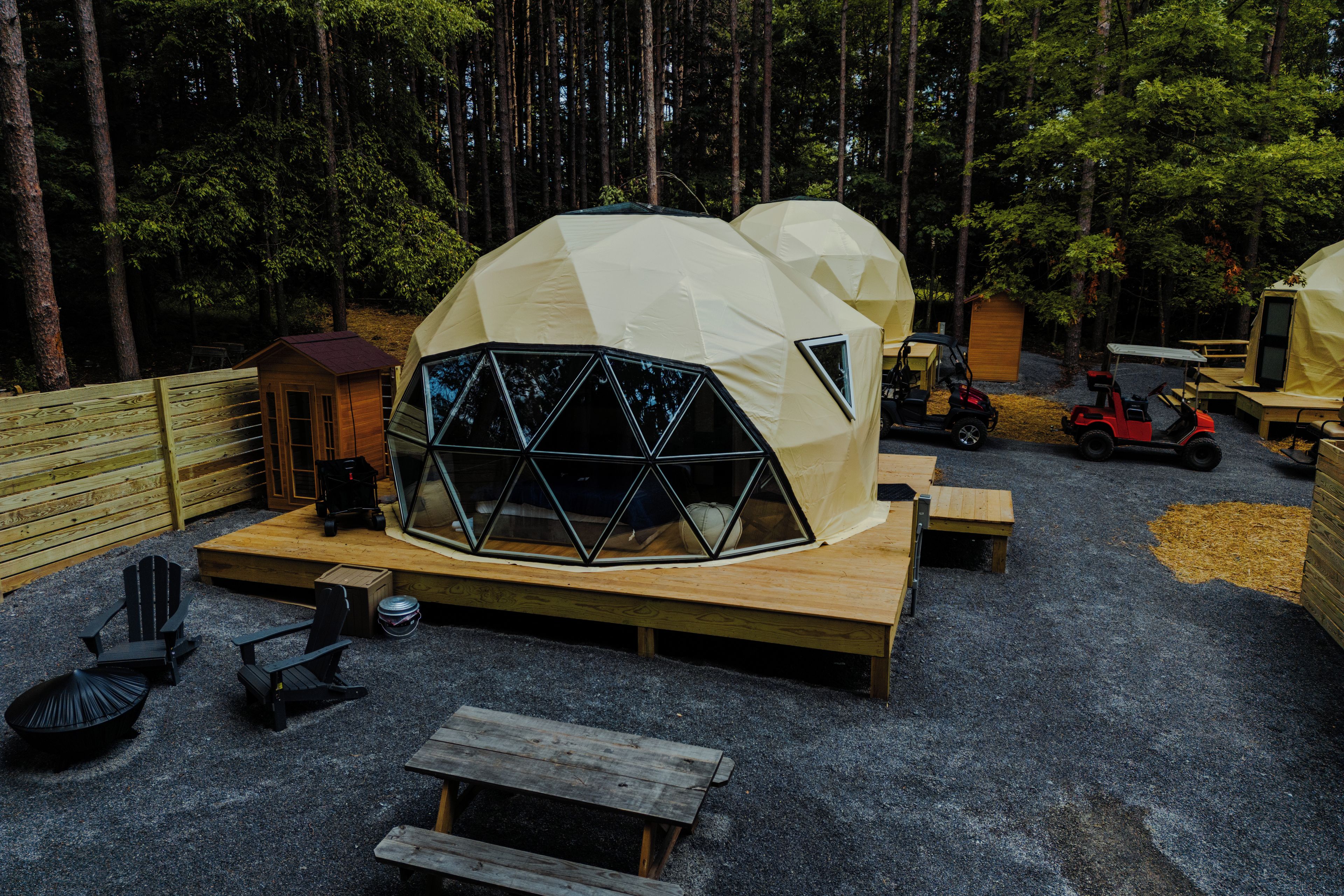 A geodesic dome structure with a wooden deck, a small wooden building, and a red golf cart.