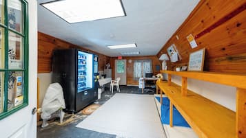 A room with wooden walls, a black refrigerator, a table with chairs, a blue mat on the floor, and a window with blinds.