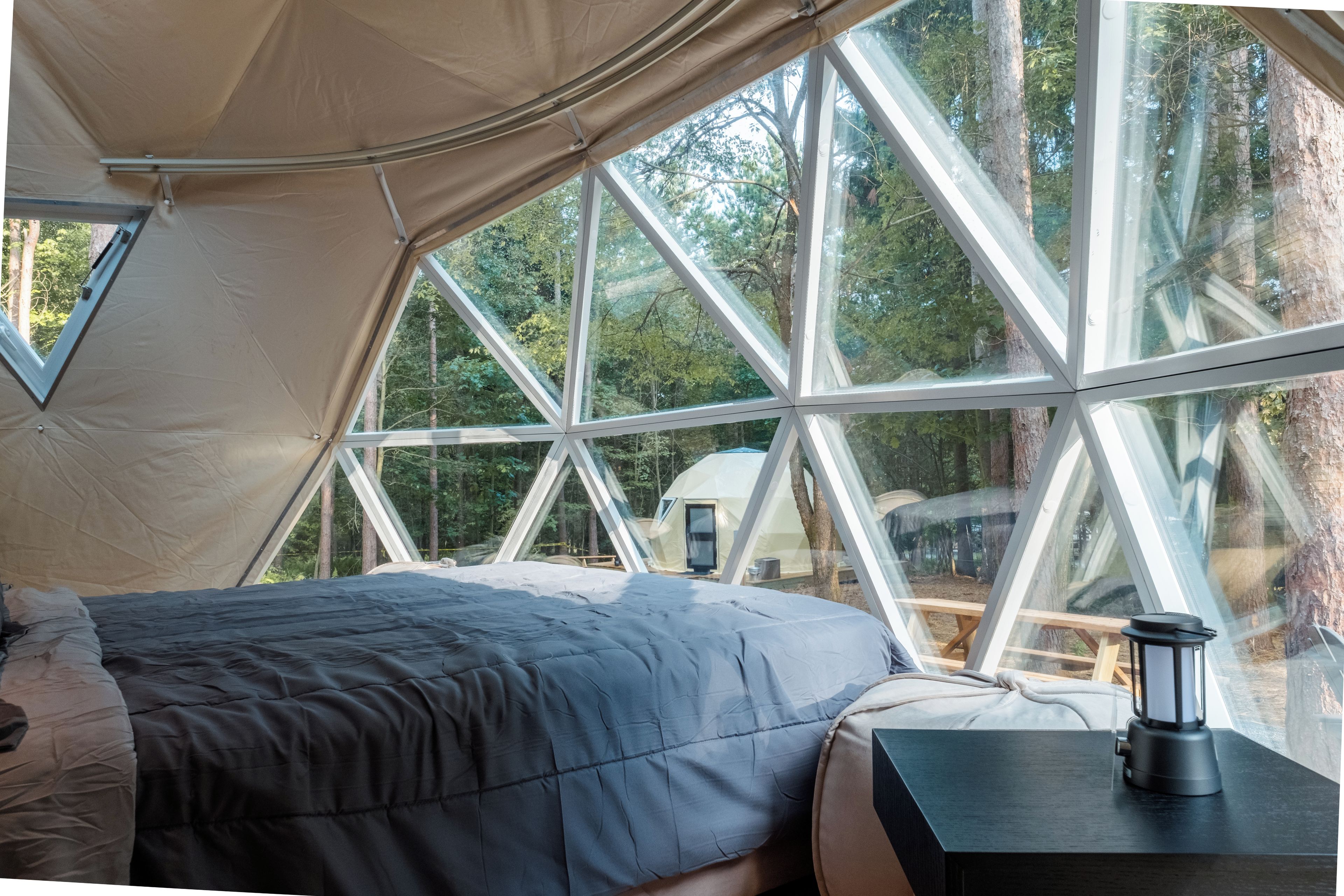 Tenda com cama e mesa, janelas amplas e vista para árvores.