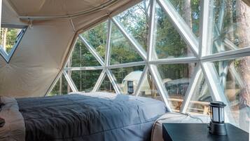 Tenda com cama e mesa, janelas amplas e vista para árvores.
