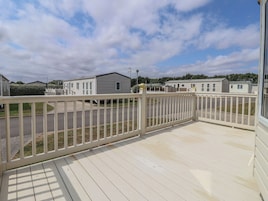 A deck with a white railing overlooking a street with mobile homes.
