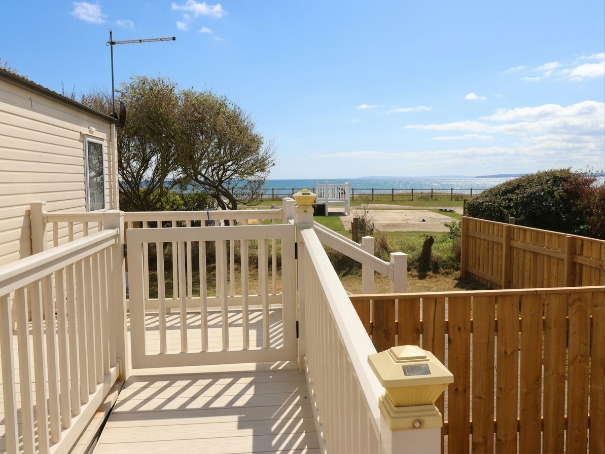 Eine Holzterrasse mit weißer Reling, Blick aufs Meer und ein klarer Himmel.