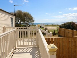 Una terraza de madera con barandilla blanca, vista al mar y cielo despejado.