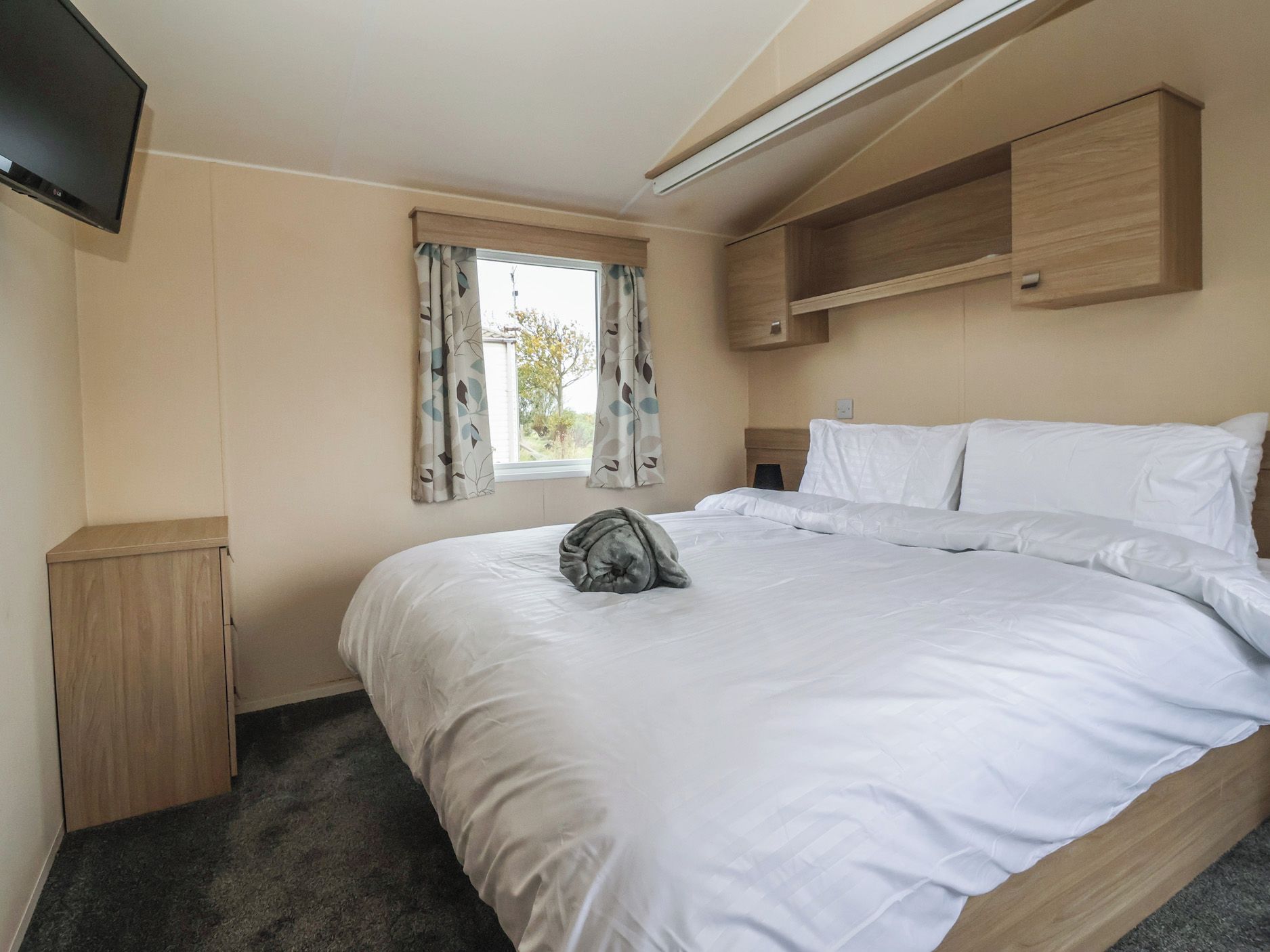 Une chambre à coucher avec un lit, une armoire, une télévision et une fenêtre avec des rideaux.