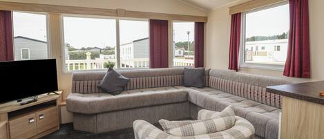 A modern living room with a sectional sofa, a television on a wooden stand, and a view of the outside through large windows.