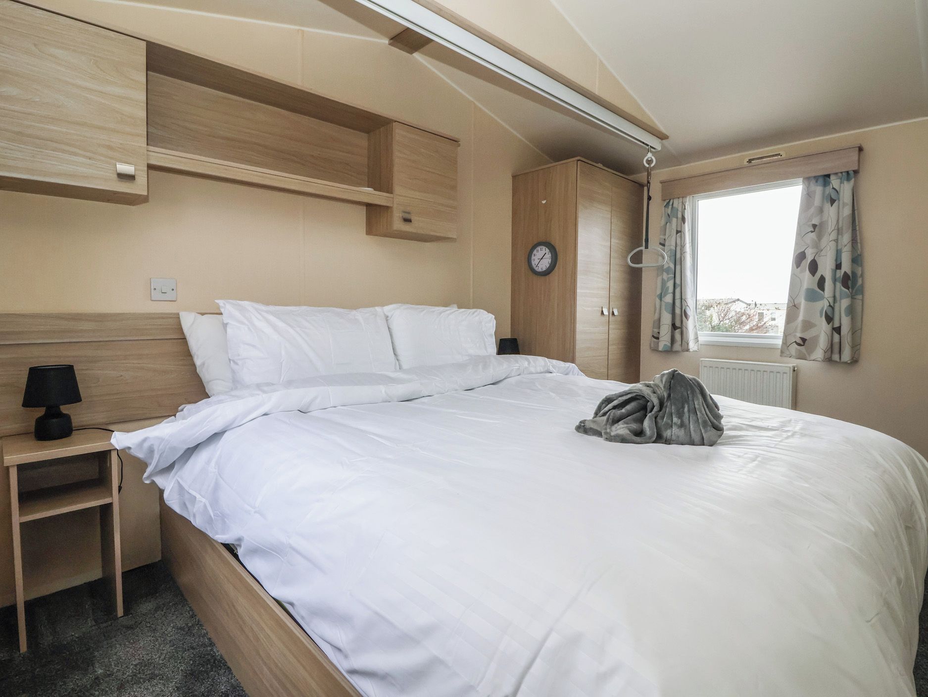 Une chambre à coucher comprenant un lit, une table de chevet, une lampe, une armoire et une fenêtre avec des rideaux.