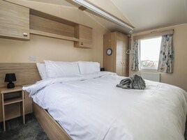 Un dormitorio con cama, mesita de noche, lámpara, armario y ventana con cortinas.