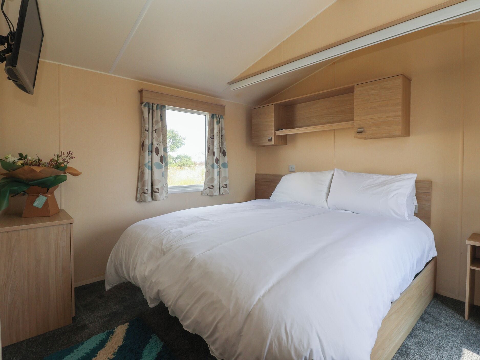 Un dormitorio con cama, escritorio, televisor y ventana con cortinas.