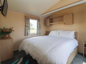 Un dormitorio con cama, escritorio, televisor y ventana con cortinas.