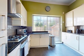 A modern kitchen with white cabinets, a gas stove, a microwave, and a stainless steel trash bin. - Amazing 2BR Flat with Garden-Easy Access to Camden (London)