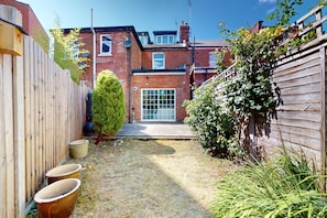 A residential backyard with a brick house, a wooden fence, a small bush, and a gravel path. - Amazing 2BR Flat with Garden-Easy Access to Camden (London)